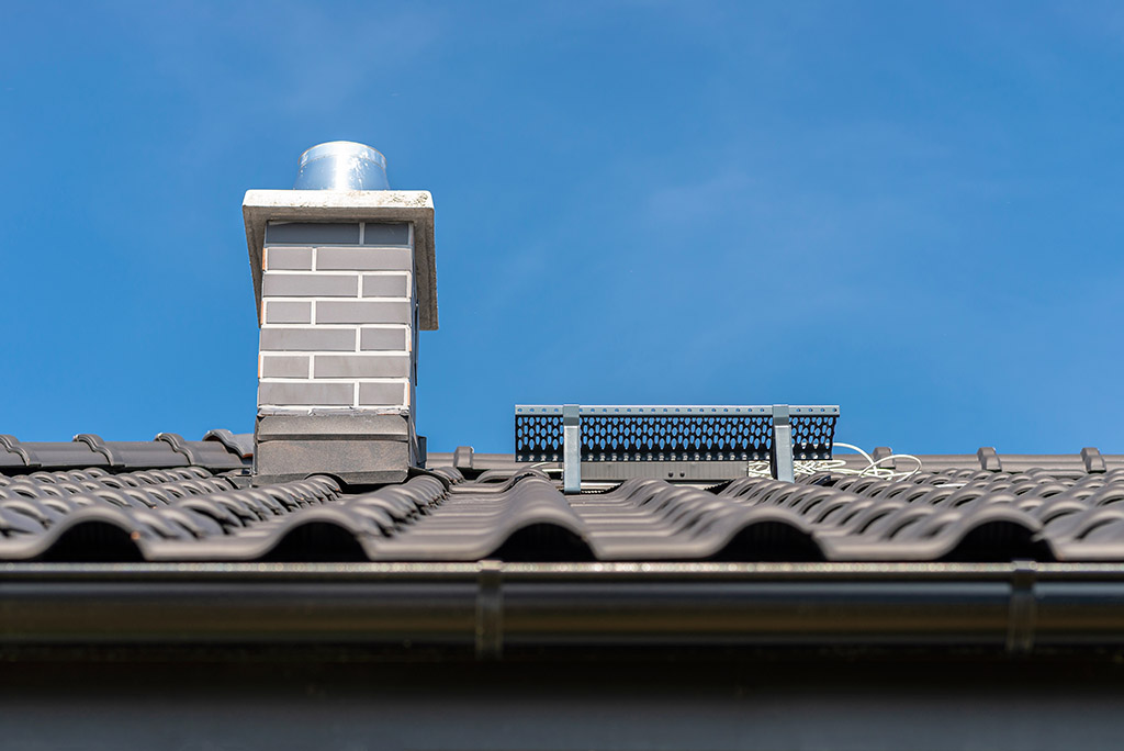 The roof of a single-family house covered with a new ceramic tile in anthracite against the blue sky. Vsible system chimney covered with tiles.